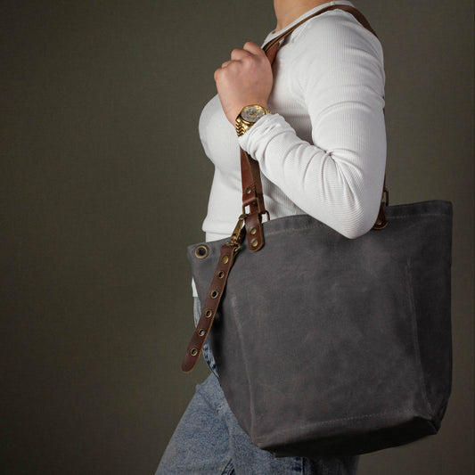 Person carrying a dark gray tote bag with leather straps against a dark background