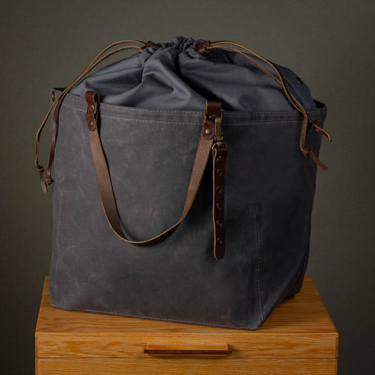Gray drawstring bag with brown leather straps on a wooden surface against a dark background