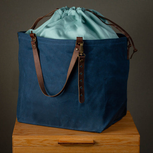 Blue tote bag with a green drawstring bag inside on a wooden surface.