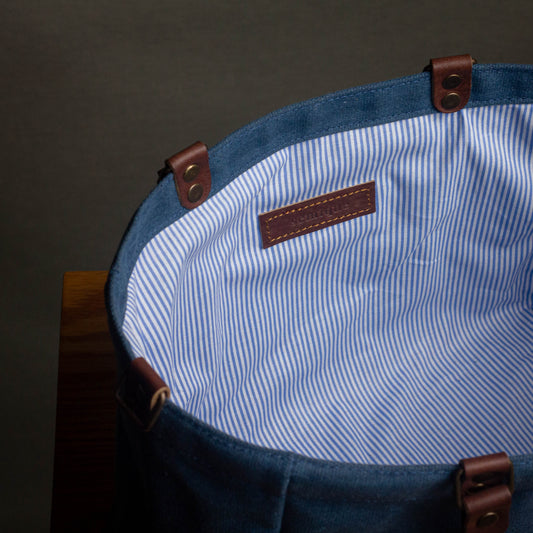 Close-up of a blue bag with a striped interior and brown leather straps on a dark background