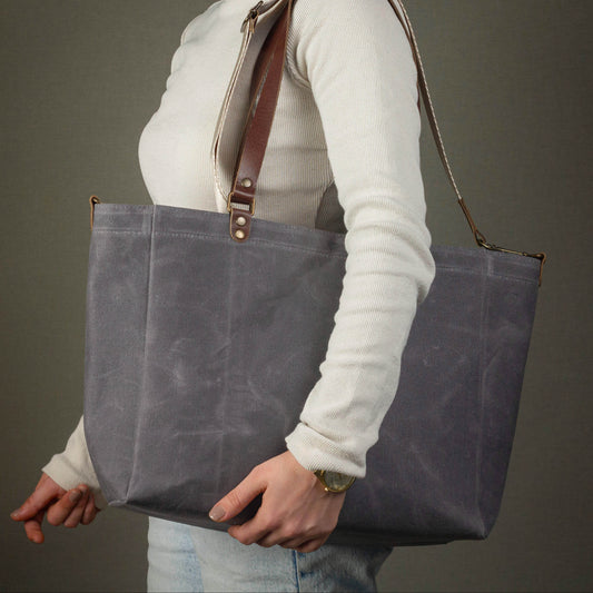 Person holding a gray tote bag with a brown strap against a neutral background
