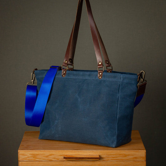Blue tote bag with brown straps on a wooden surface against a dark background