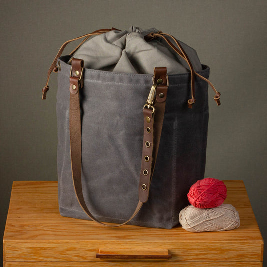 Gray drawstring bag with brown straps on a wooden surface against a gray background