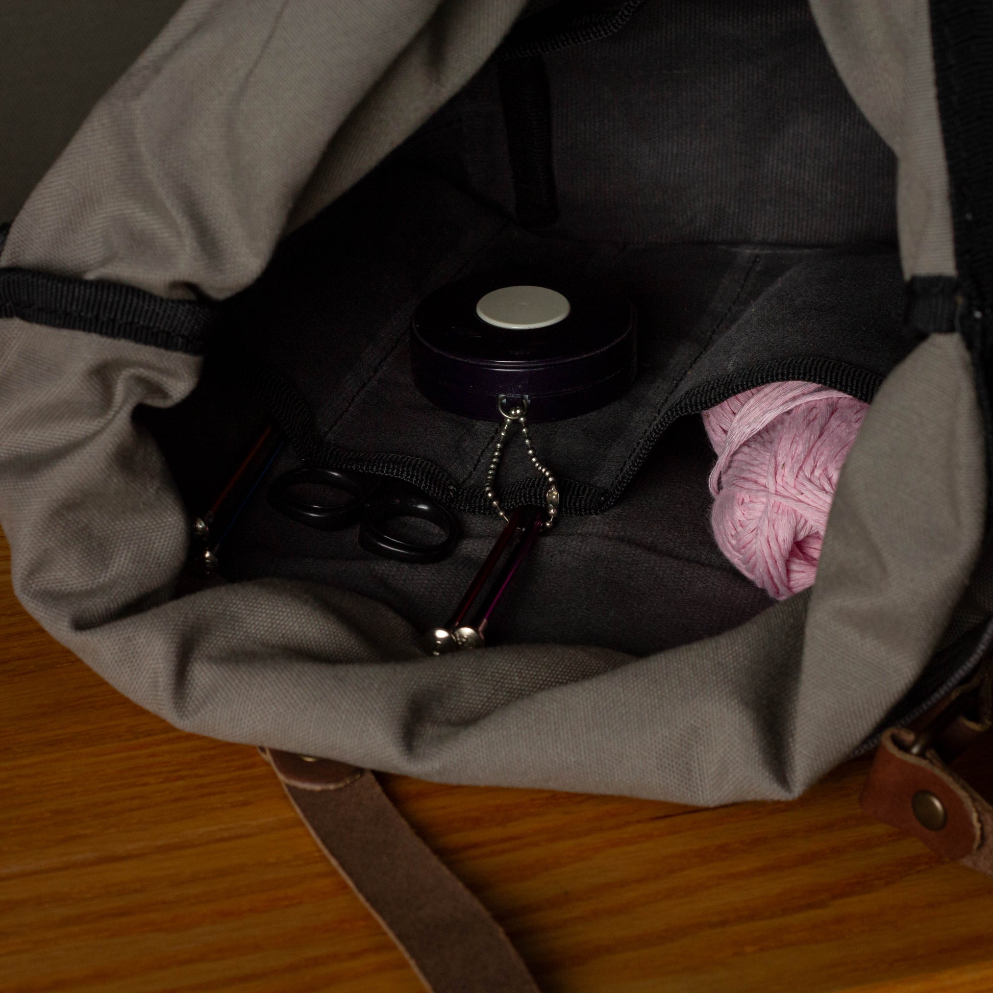 Open bag containing a pink item, black container, and other small objects on a wooden surface.