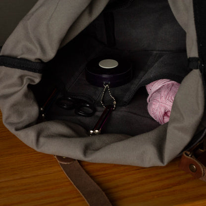 Open bag containing a pink item, black container, and other small objects on a wooden surface.