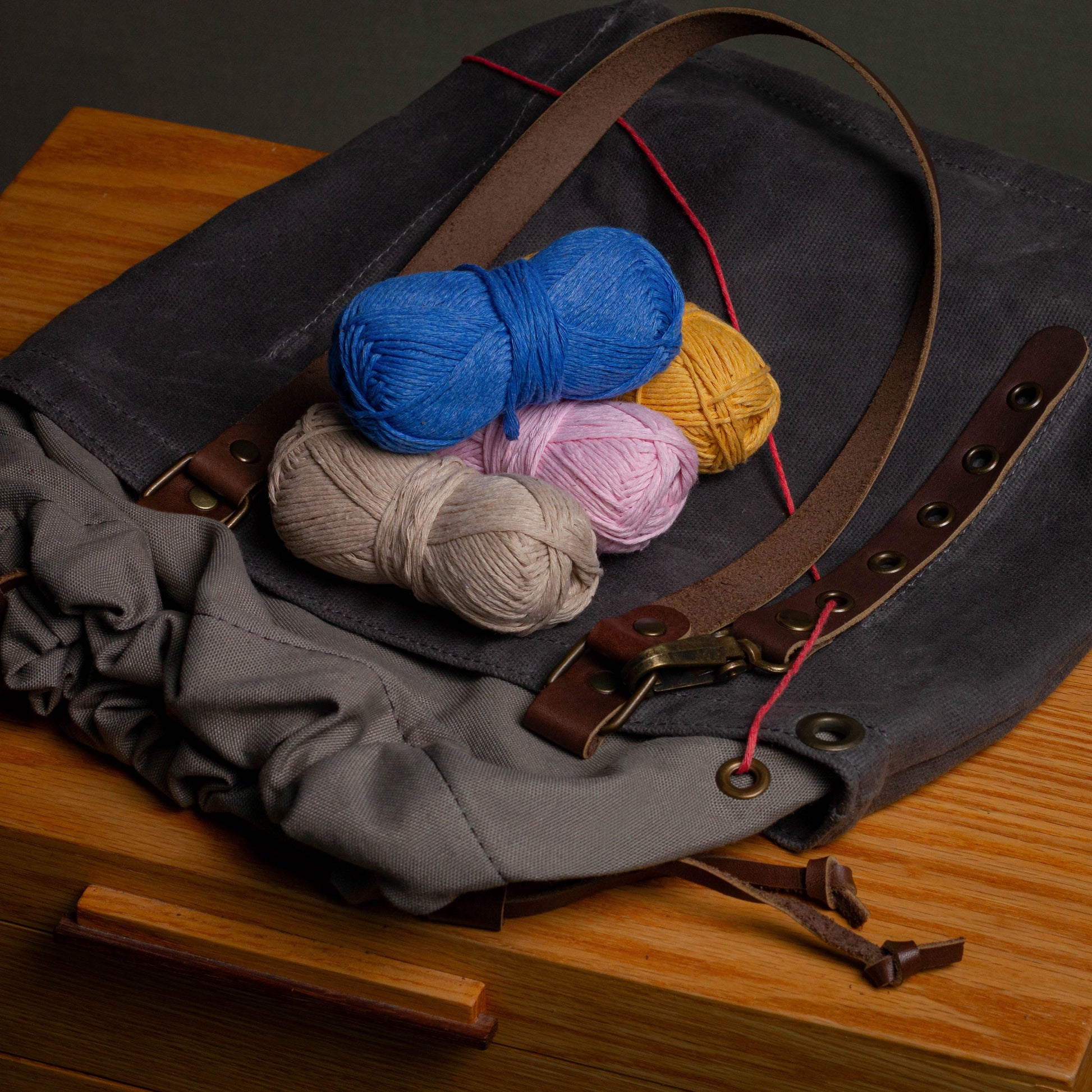 Yarn balls on a dark fabric bag with leather straps on a wooden surface