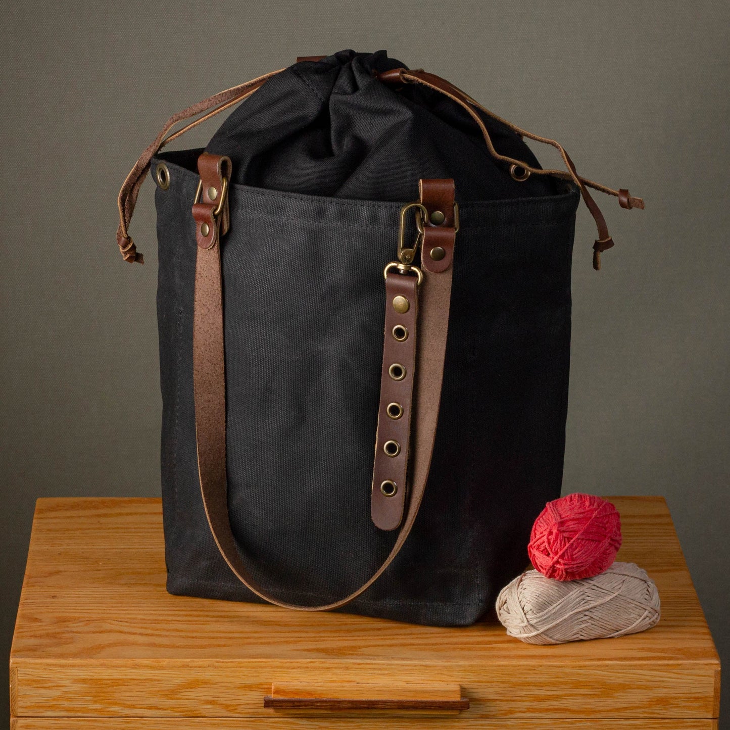 Black canvas bag with brown leather straps on a wooden surface against a gray background