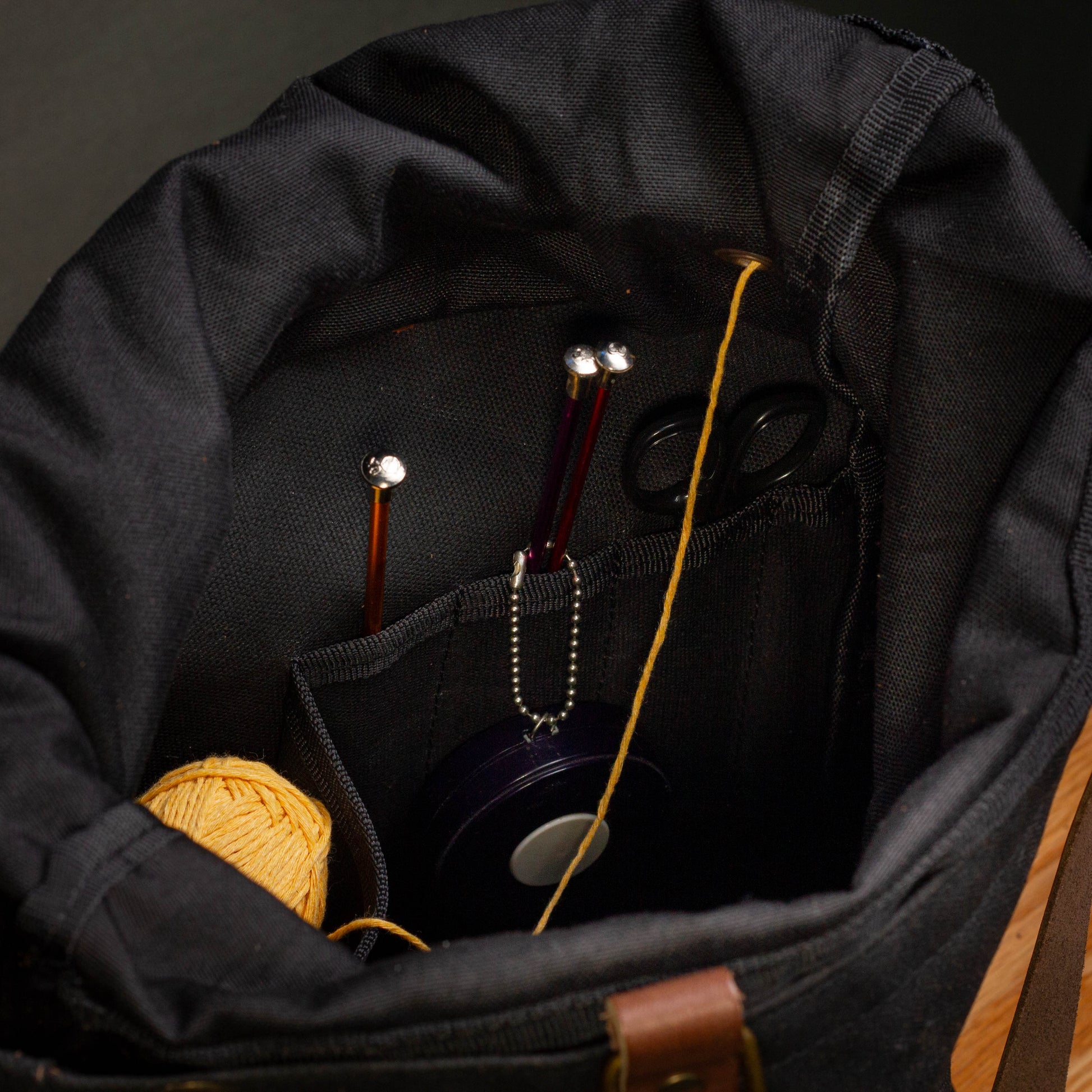 Black bag with knitting supplies including yarn, needles, and scissors on a dark background