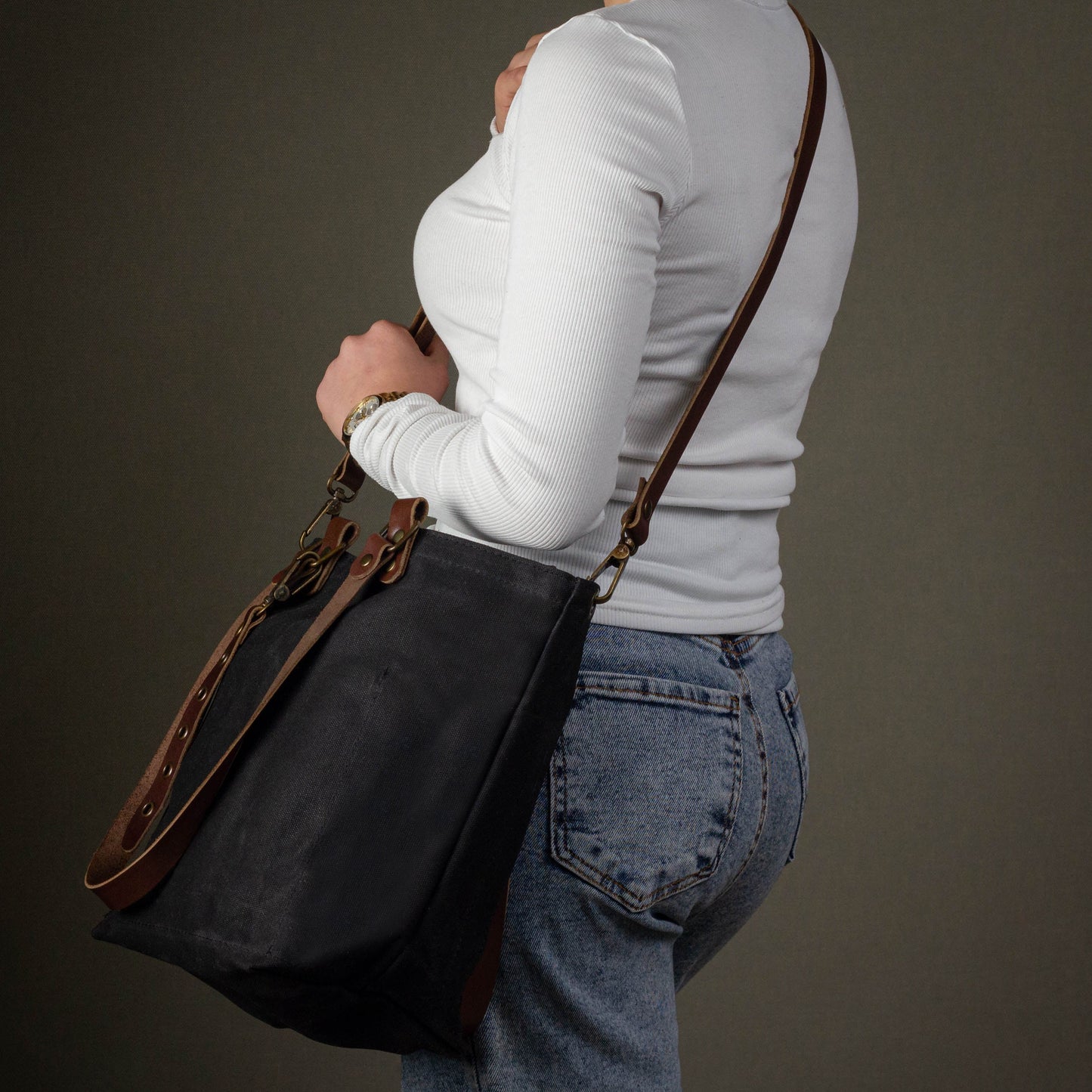 Person wearing a black shoulder bag with brown straps on a dark background