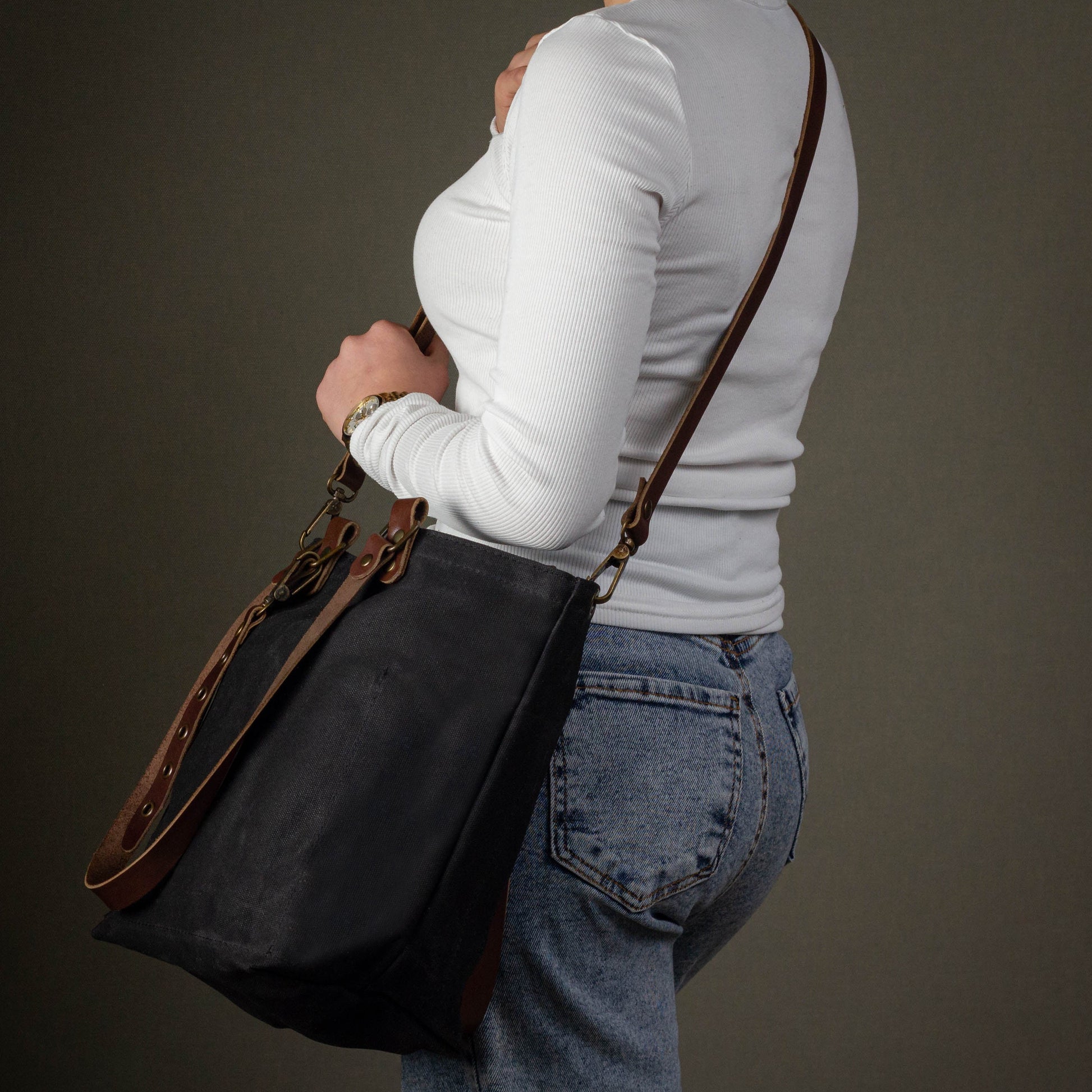 Person wearing a black shoulder bag with brown straps on a dark background