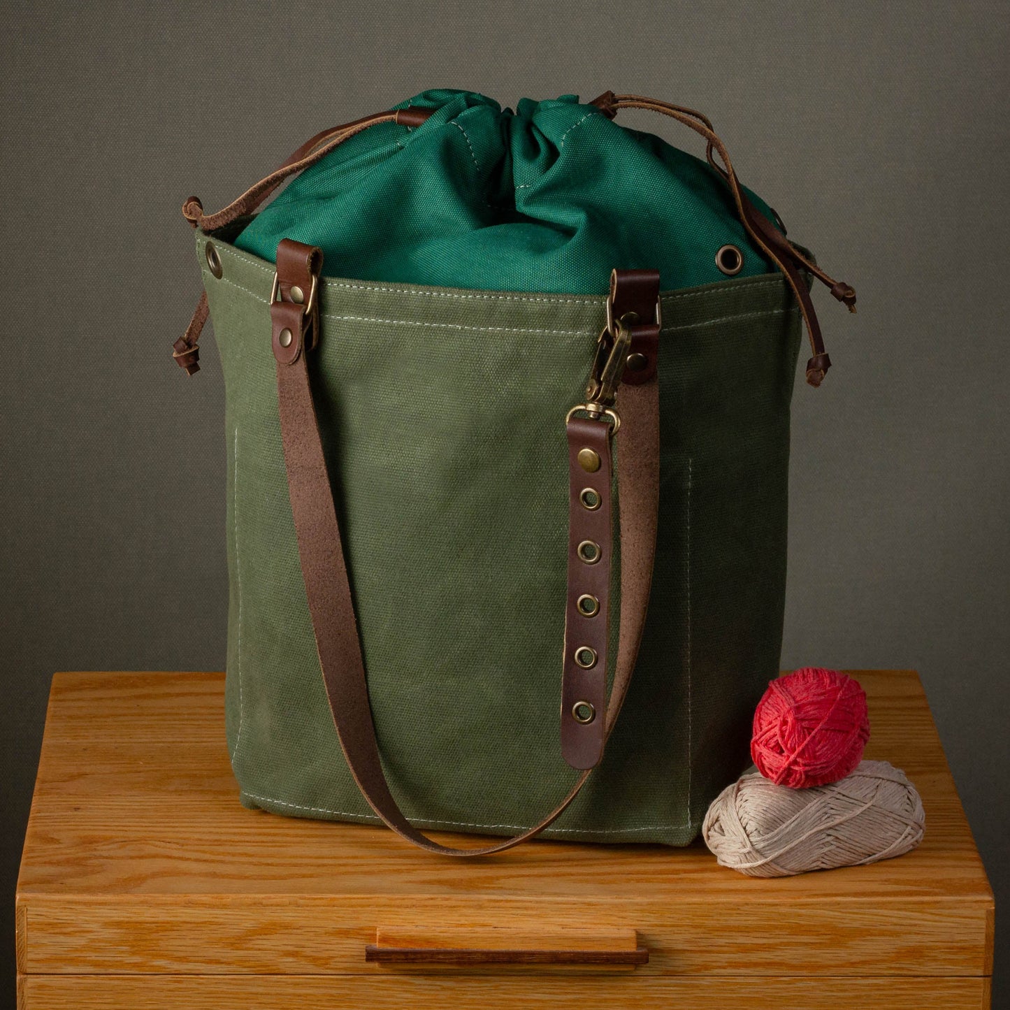 Green canvas bag with brown leather straps on a wooden surface against a gray background