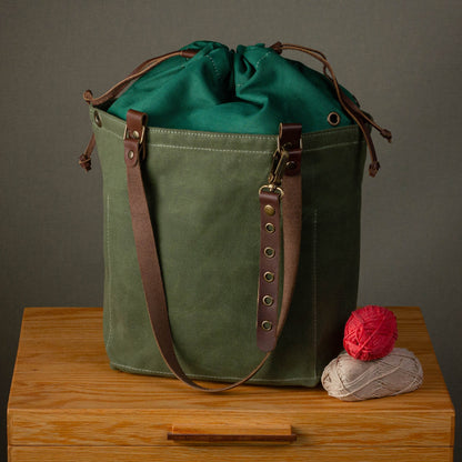 Green canvas bag with brown leather straps on a wooden surface against a gray background
