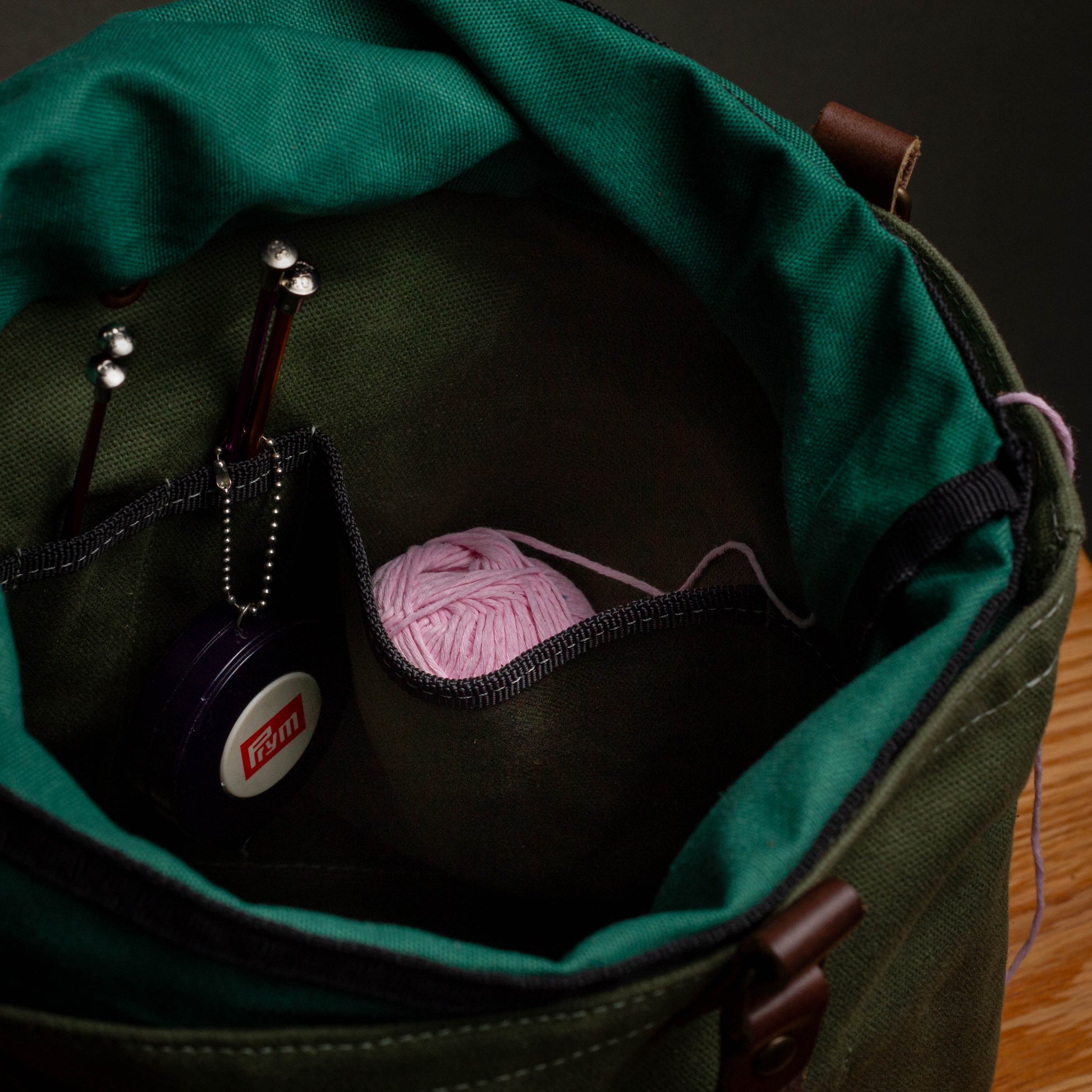 Green bag with pink yarn and knitting needles on a wooden surface