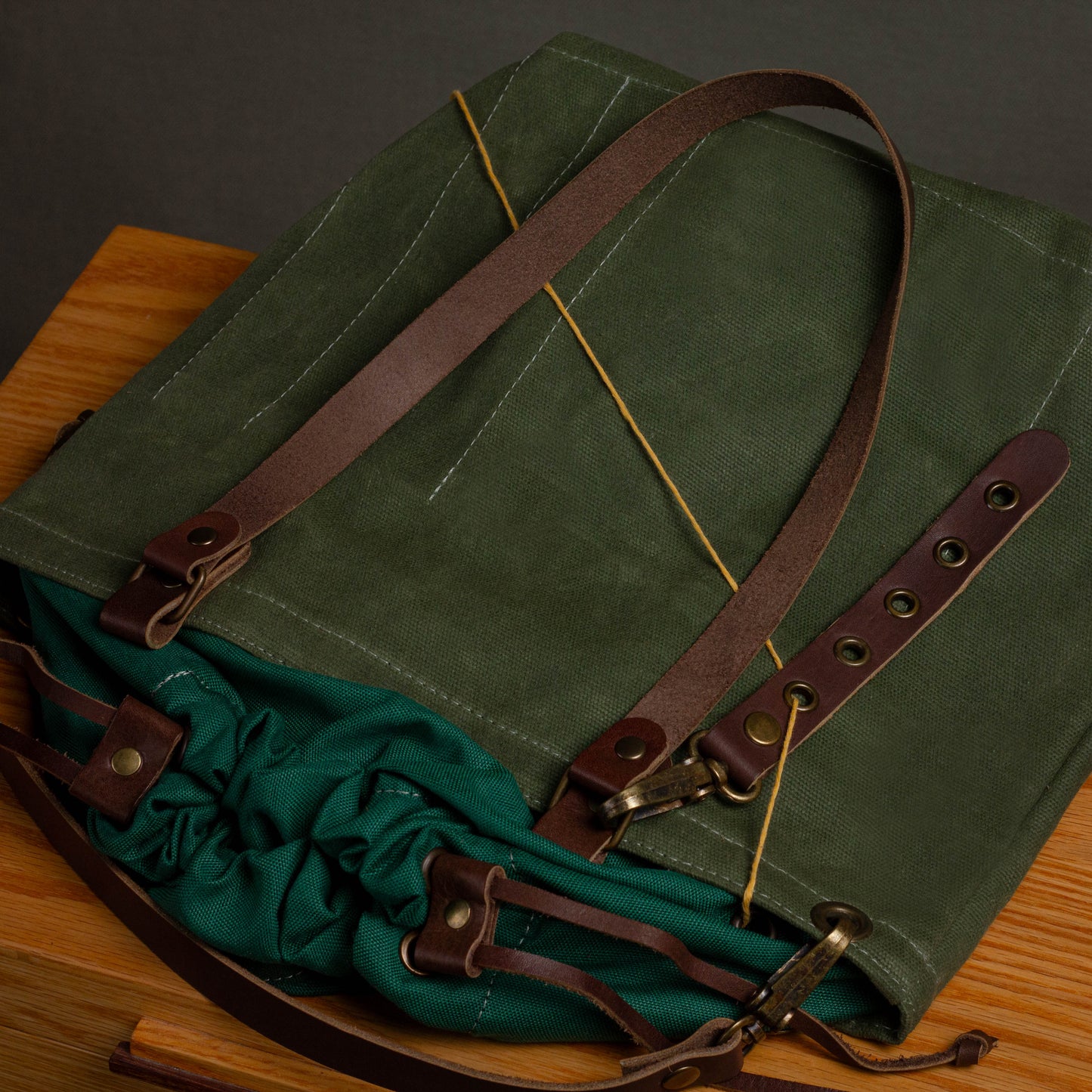 Green waxed canvas bag with brown leather straps on a wooden surface