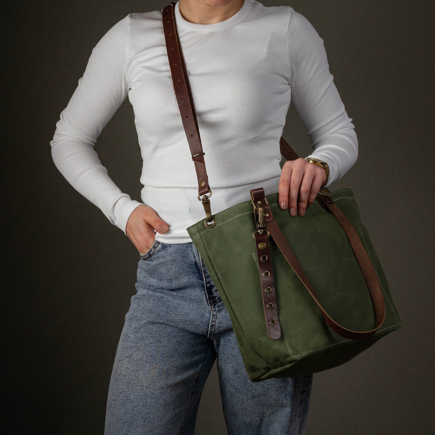 Person holding a green bag with brown straps against a dark background