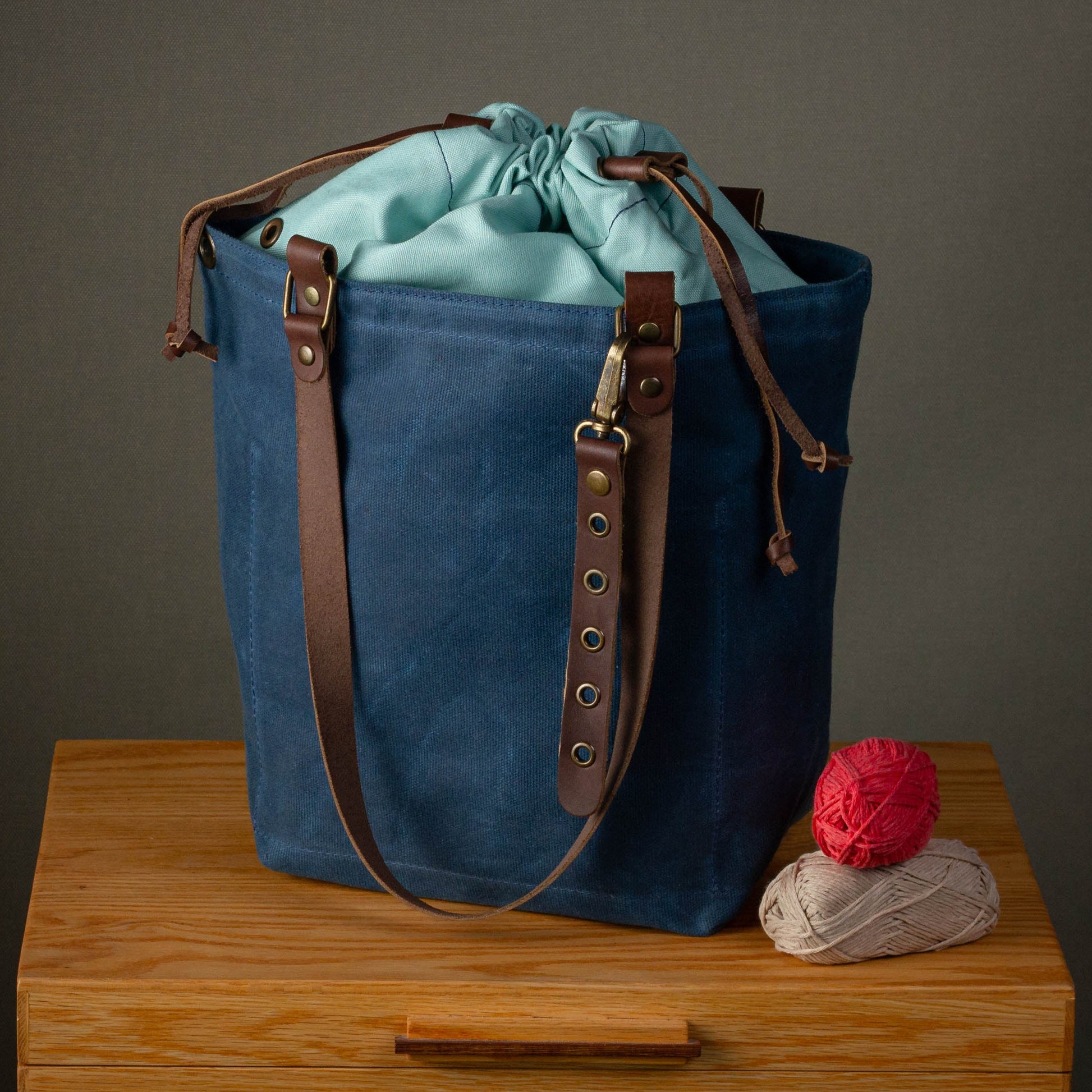 Blue canvas bag with brown leather straps on a wooden surface against a gray background