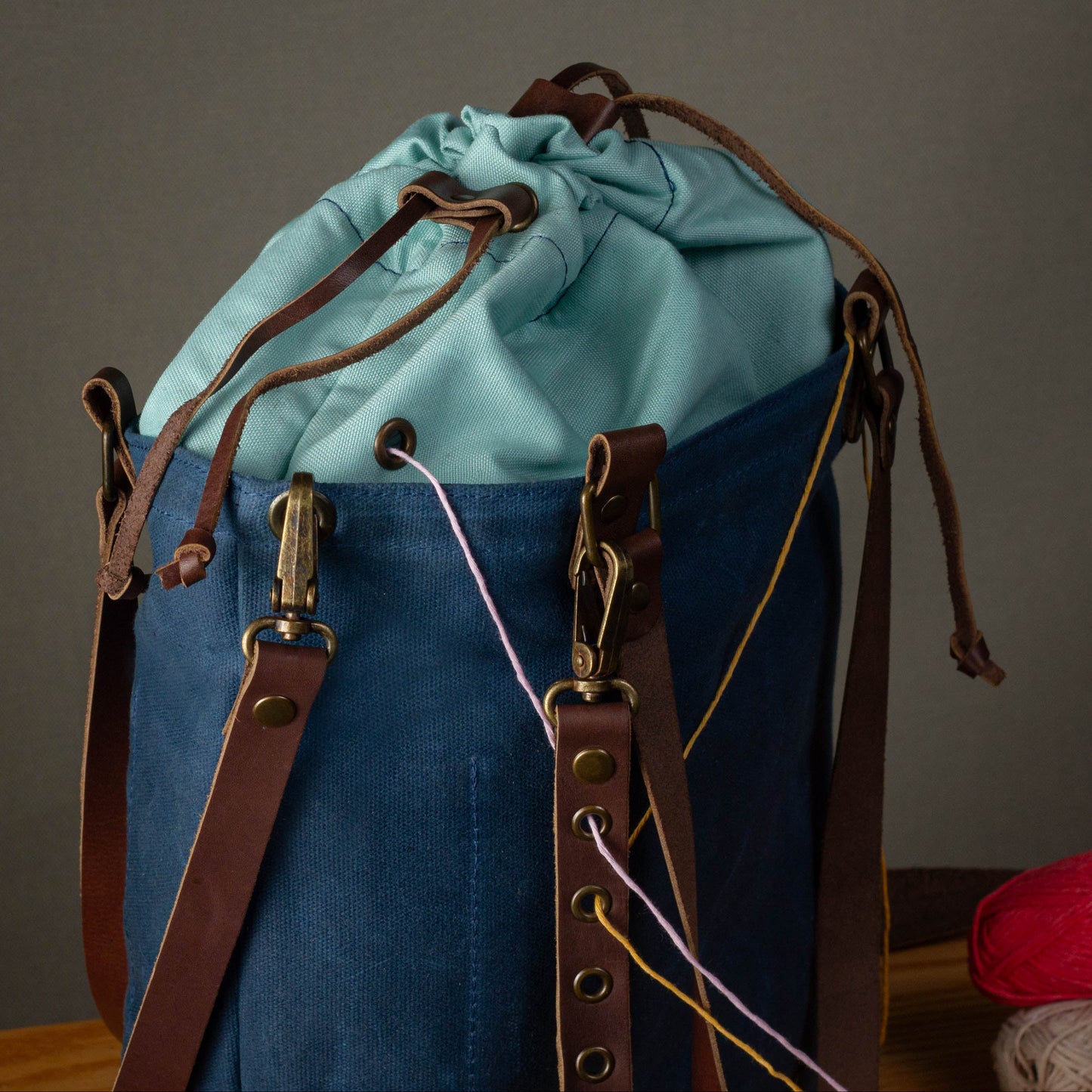 Blue and green drawstring bag with leather straps on a gray background