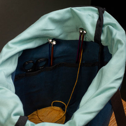 Knitting needles and yarn inside a teal drawstring bag on a dark background