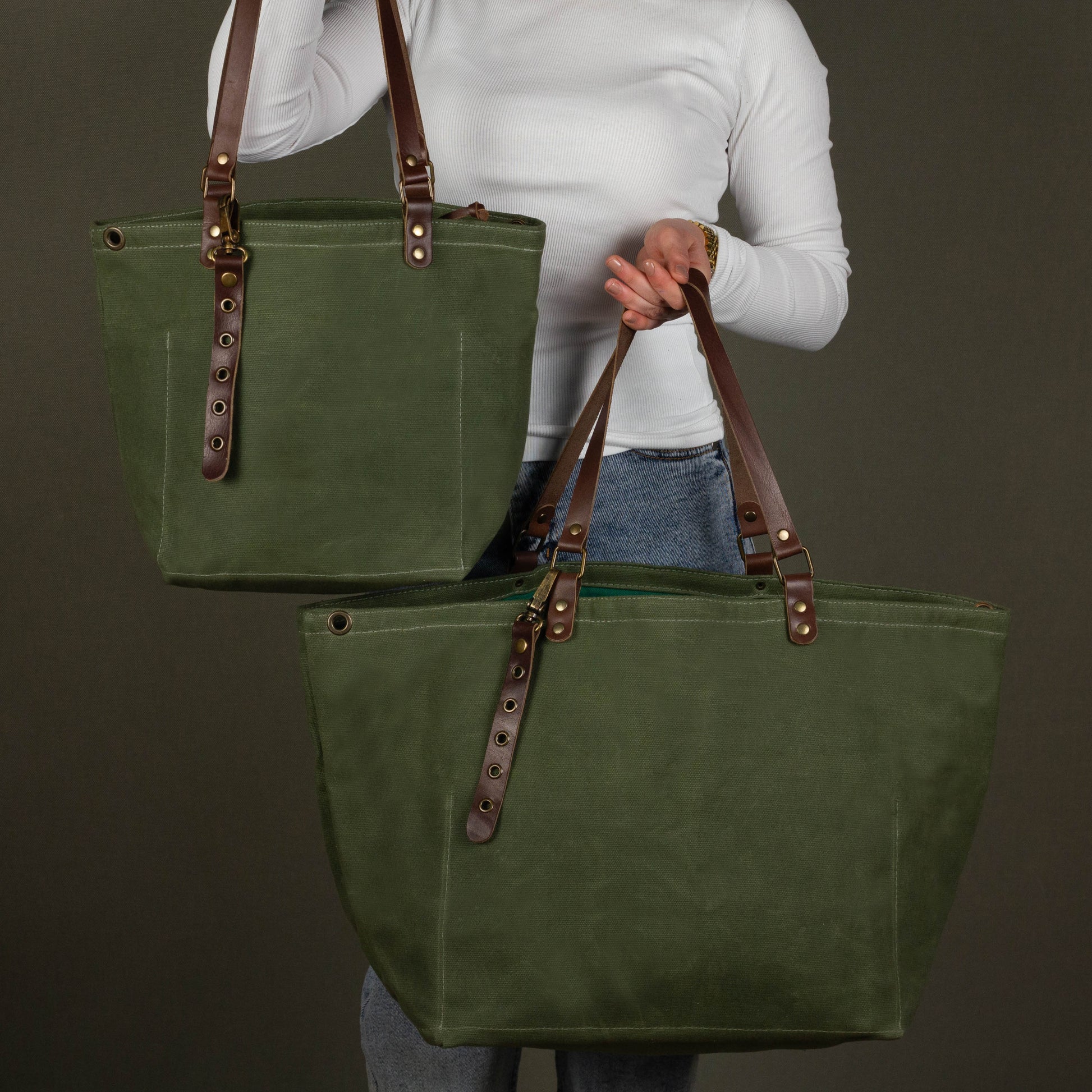 Green tote bag with brown straps held by a person against a dark background