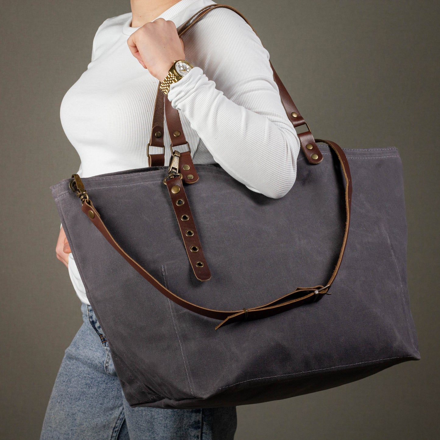 Person holding a gray tote bag with brown leather straps against a neutral background
