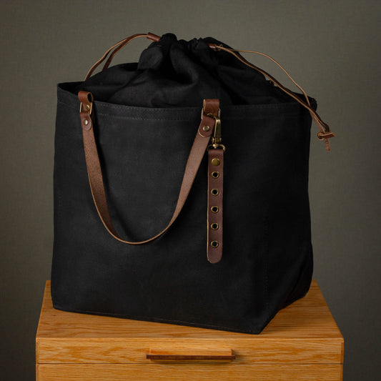 Black tote bag with brown leather straps on a wooden surface against a gray background