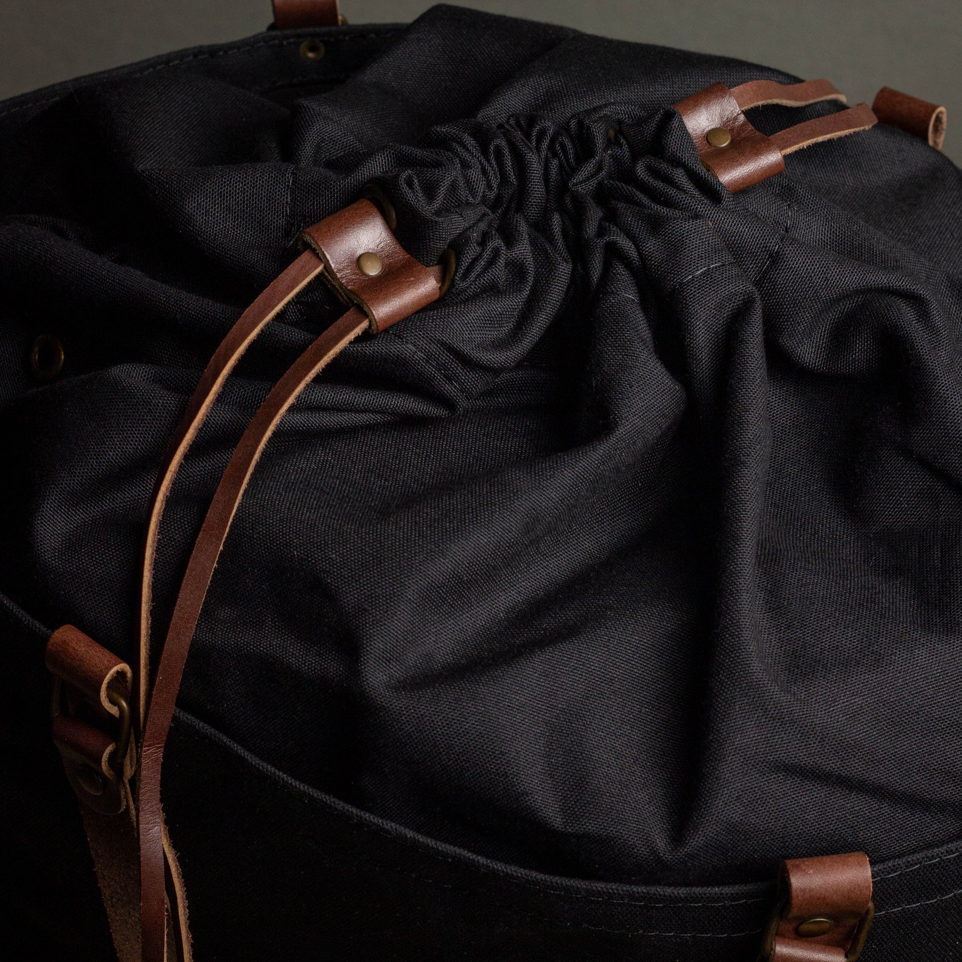 Black drawstring bag with brown leather straps on a dark background