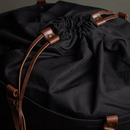 Black drawstring bag with brown leather straps on a dark background
