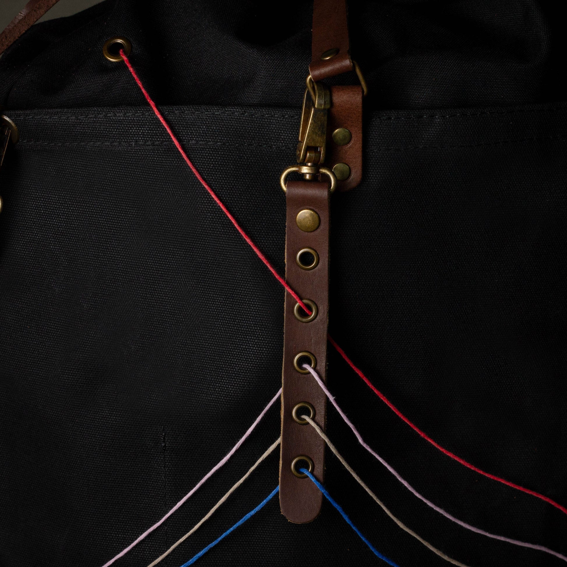 Close-up of a black bag with a brown leather strap and colorful strings.