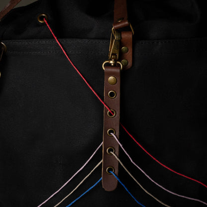 Close-up of a black bag with a brown leather strap and colorful strings.