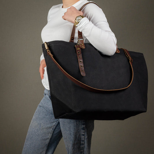 Person holding a black bag with brown straps against a gray background