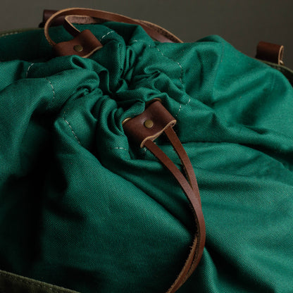 Green drawstring bag with brown leather straps on a dark background