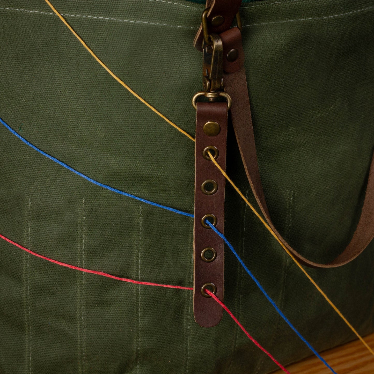 Green bag with a brown leather strap and colorful strings.