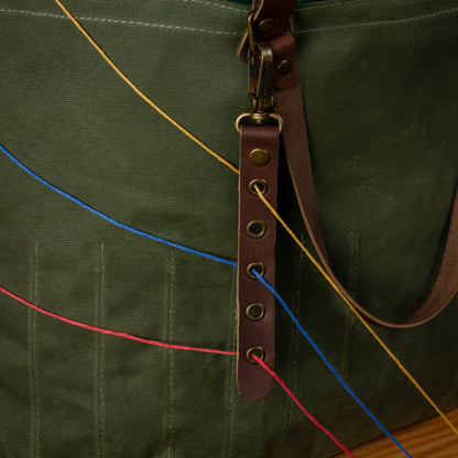 Green bag with a brown leather strap and colorful strings.
