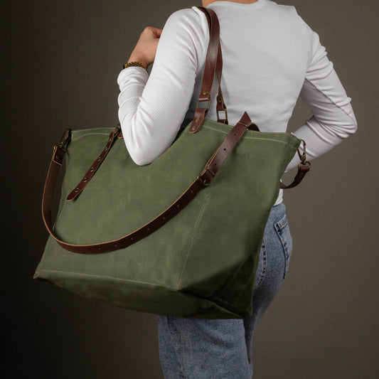 Person holding a green tote bag with brown straps against a dark background