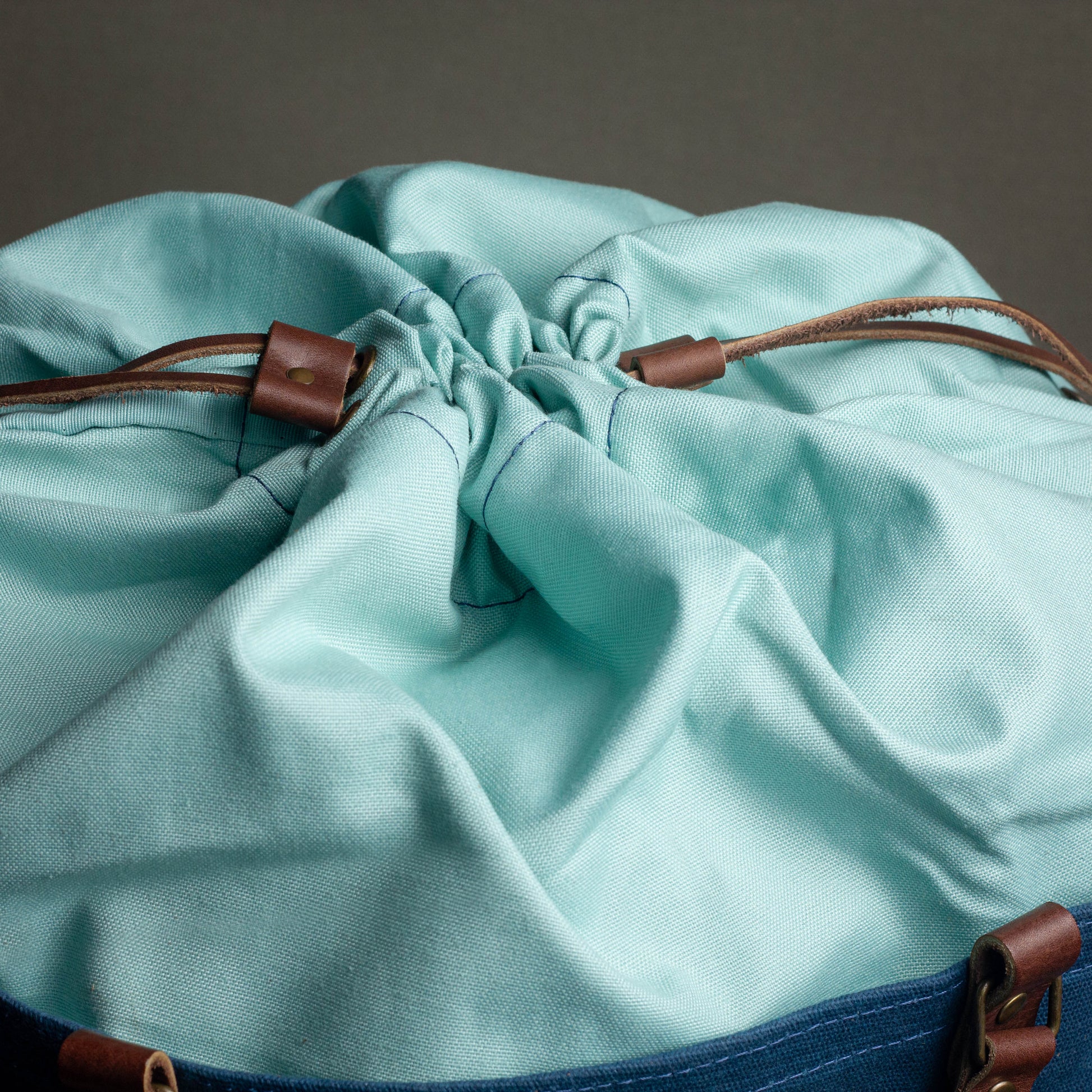 Close-up of a light blue drawstring bag with brown leather straps on a dark background