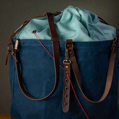 Blue bag with brown straps and a red string on a gray background