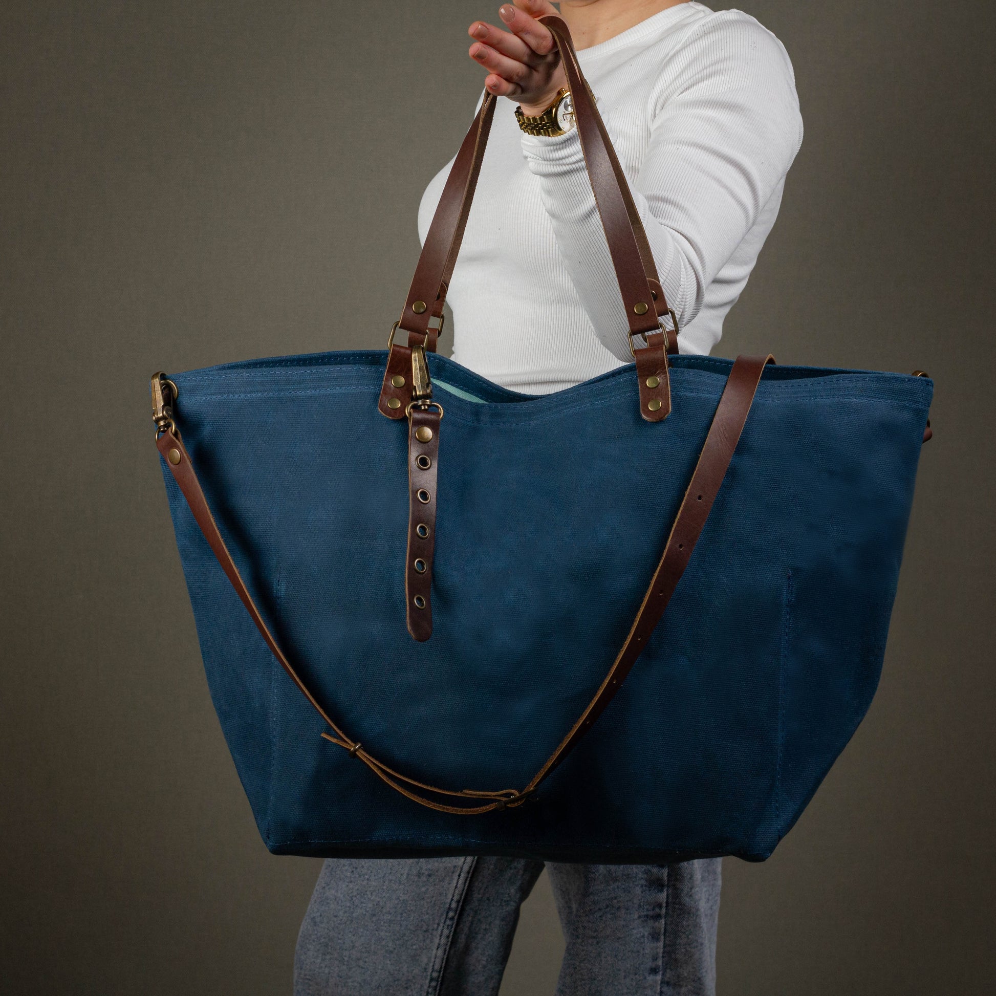 Person holding a blue tote bag with brown straps against a gray background
