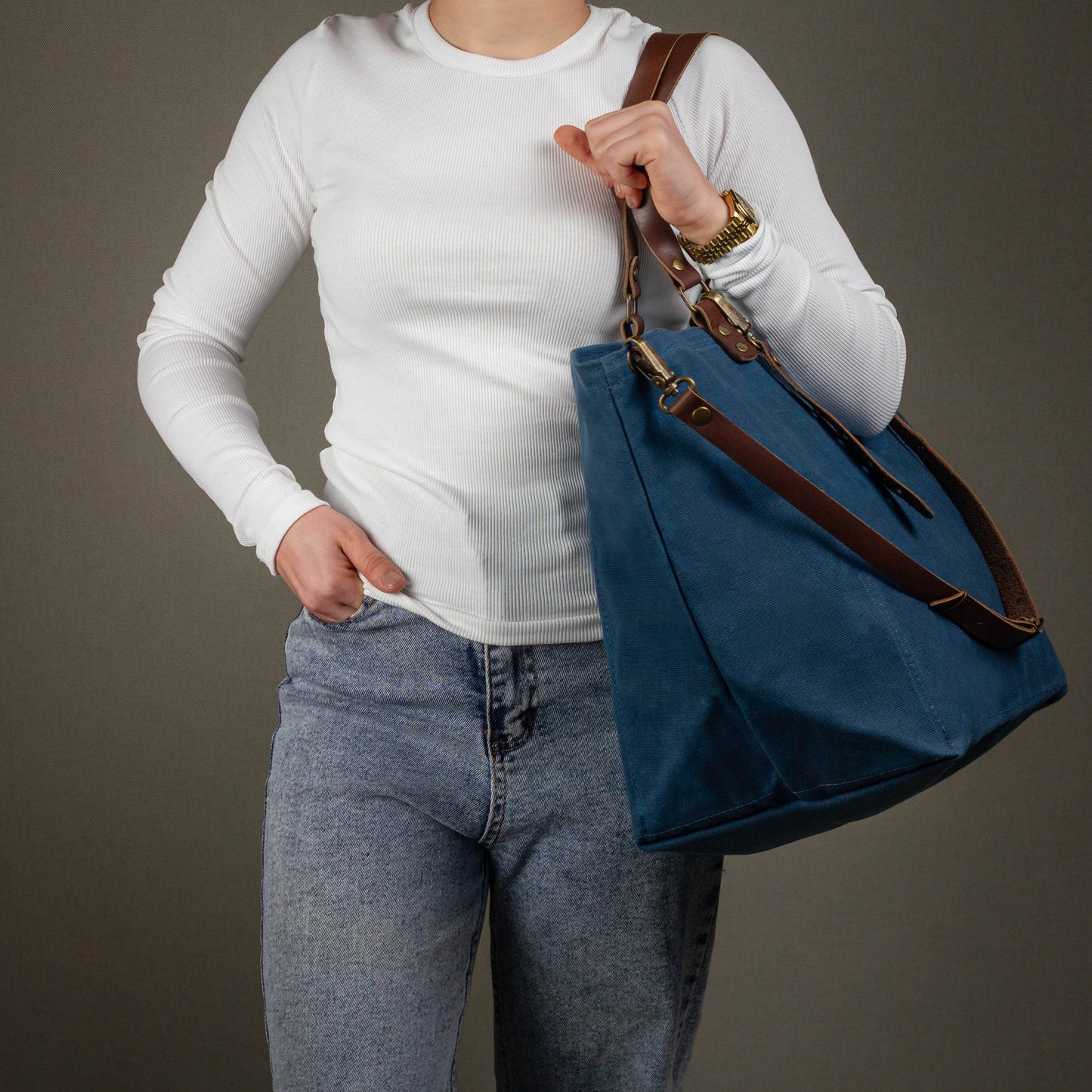 Person holding a blue tote bag with brown straps against a plain background