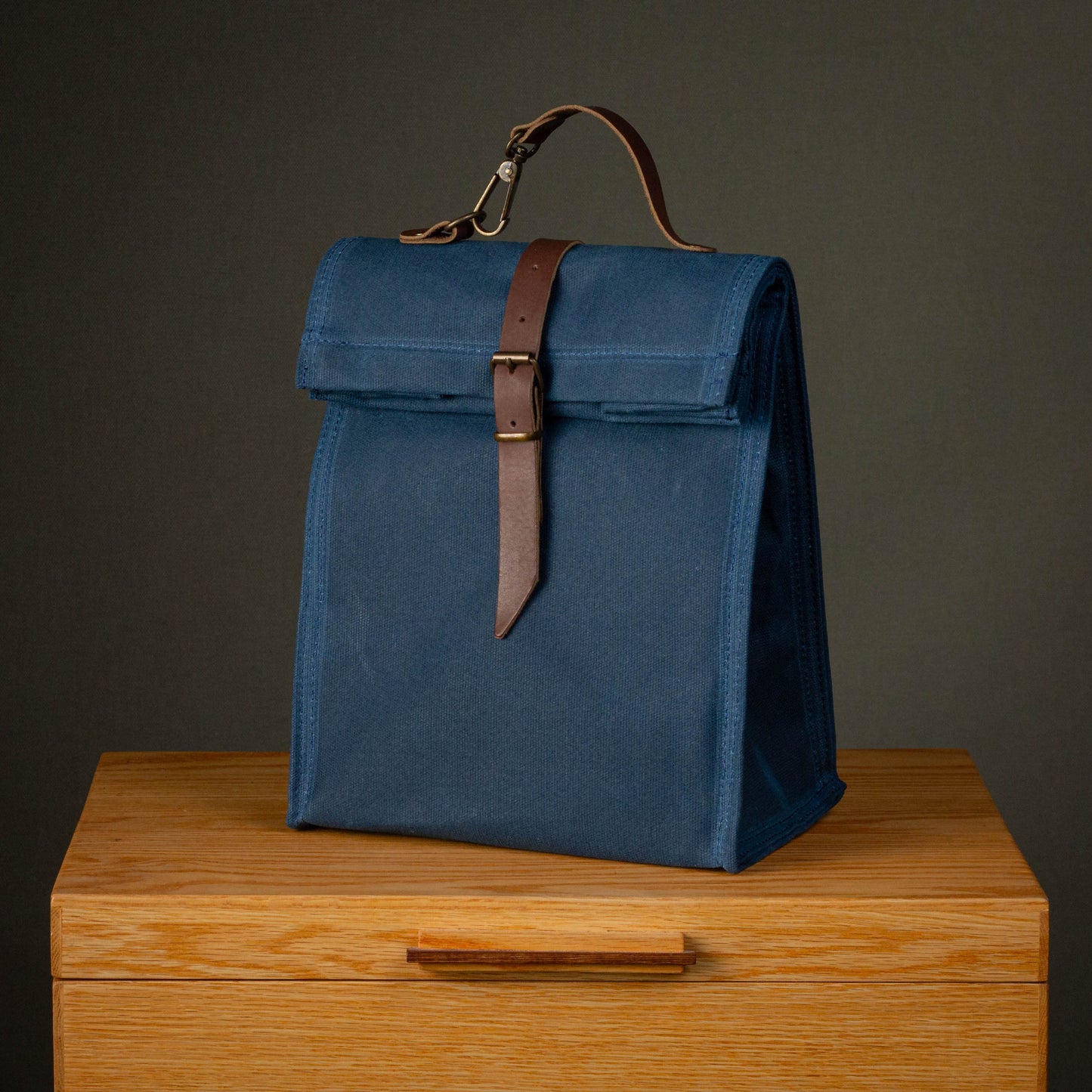 Blue fabric bag with leather strap on a wooden surface against a dark background