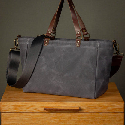 Gray tote bag with brown leather straps on a wooden surface against a dark background