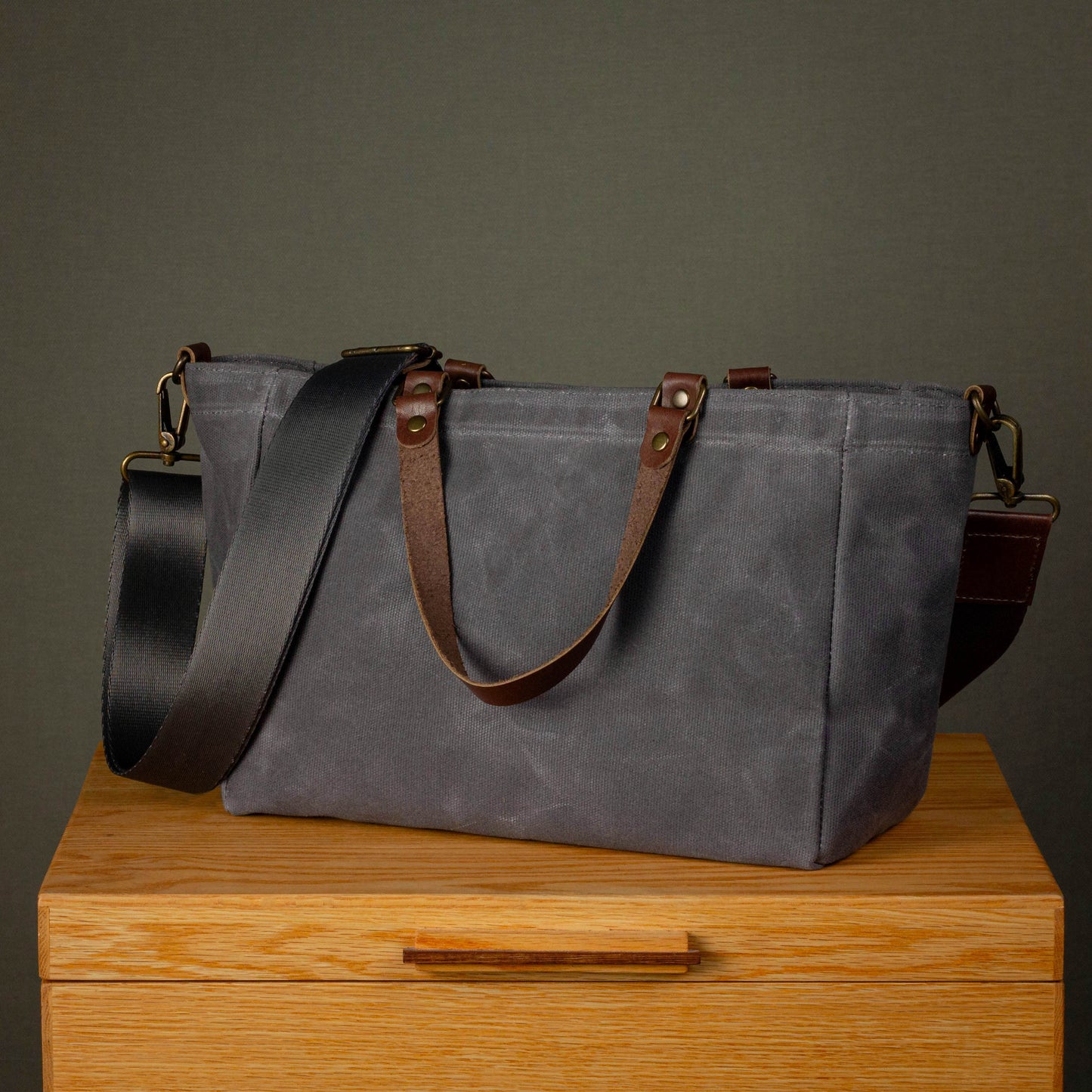 Gray tote bag with brown straps on a wooden surface against a dark background