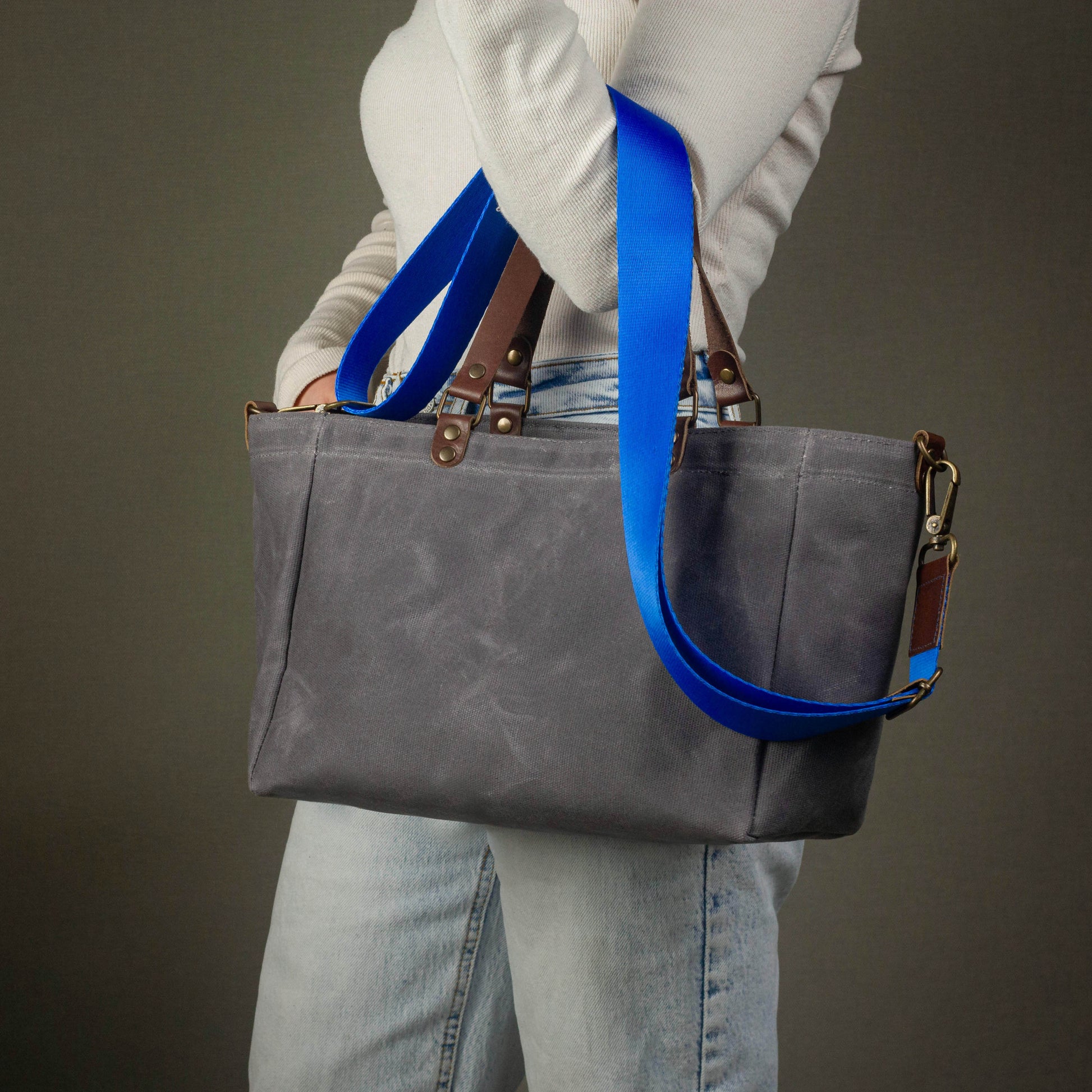 Person holding a gray tote bag with blue straps against a neutral background
