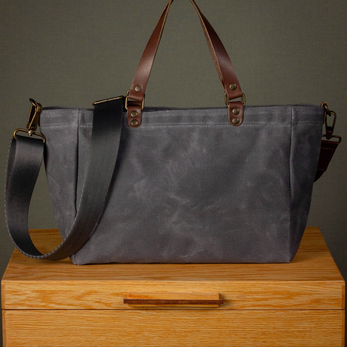 Gray tote bag with brown straps on a wooden surface against a dark background