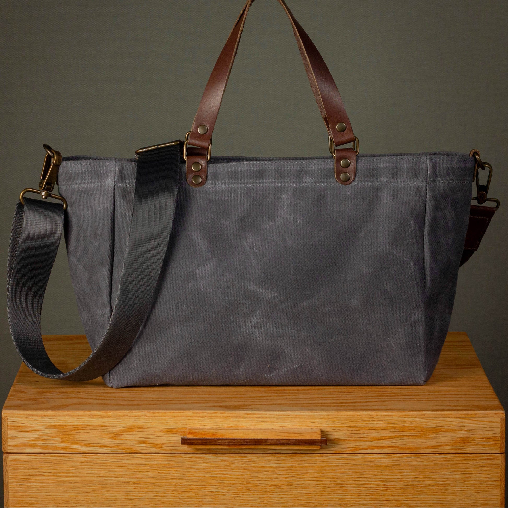 Gray tote bag with brown straps on a wooden surface against a dark background