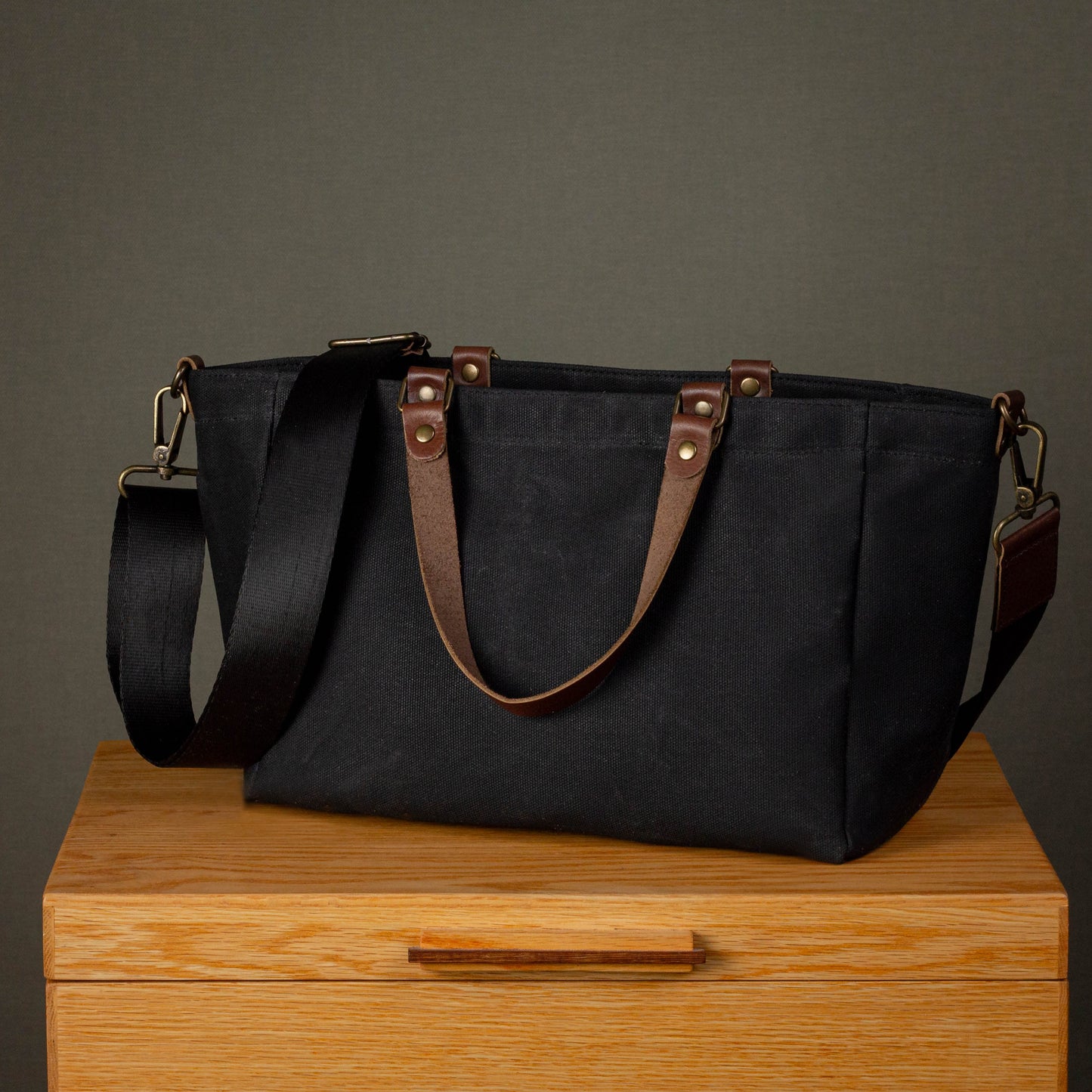 Black tote bag with brown straps on a wooden surface against a gray background