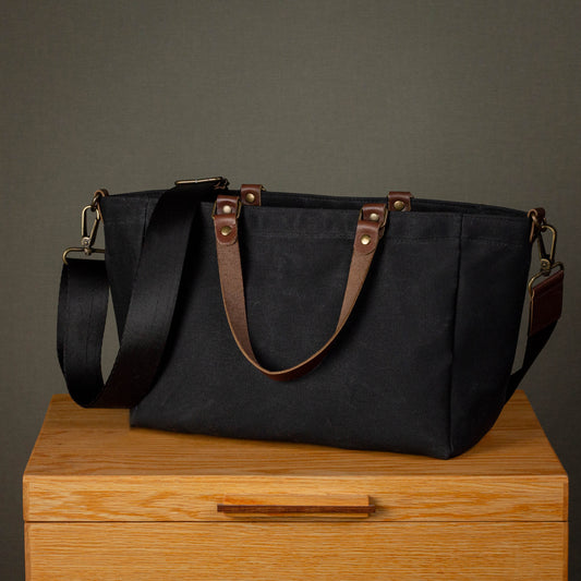 Black tote bag with brown straps on a wooden surface against a gray background