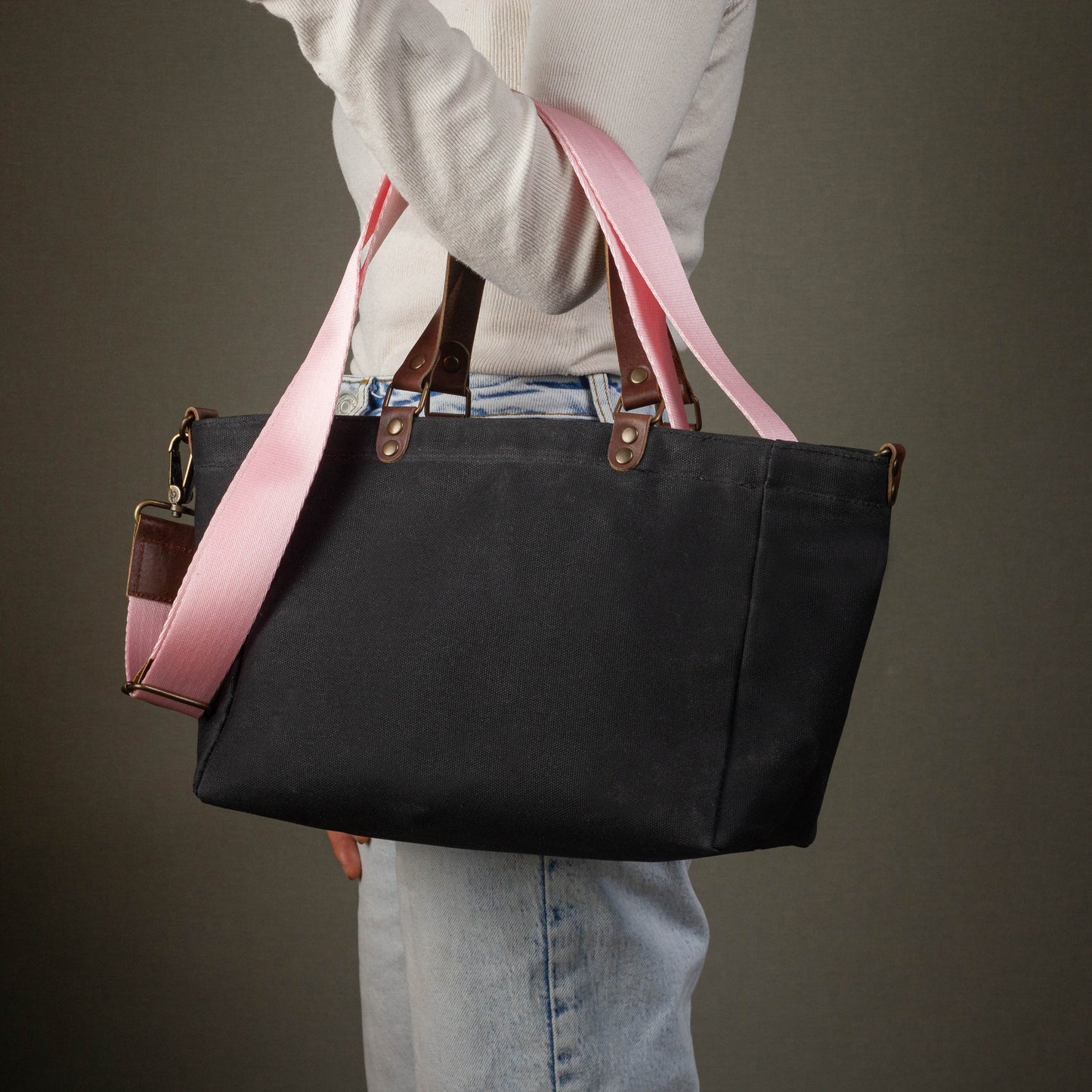 Person holding a black tote bag with pink straps against a dark background