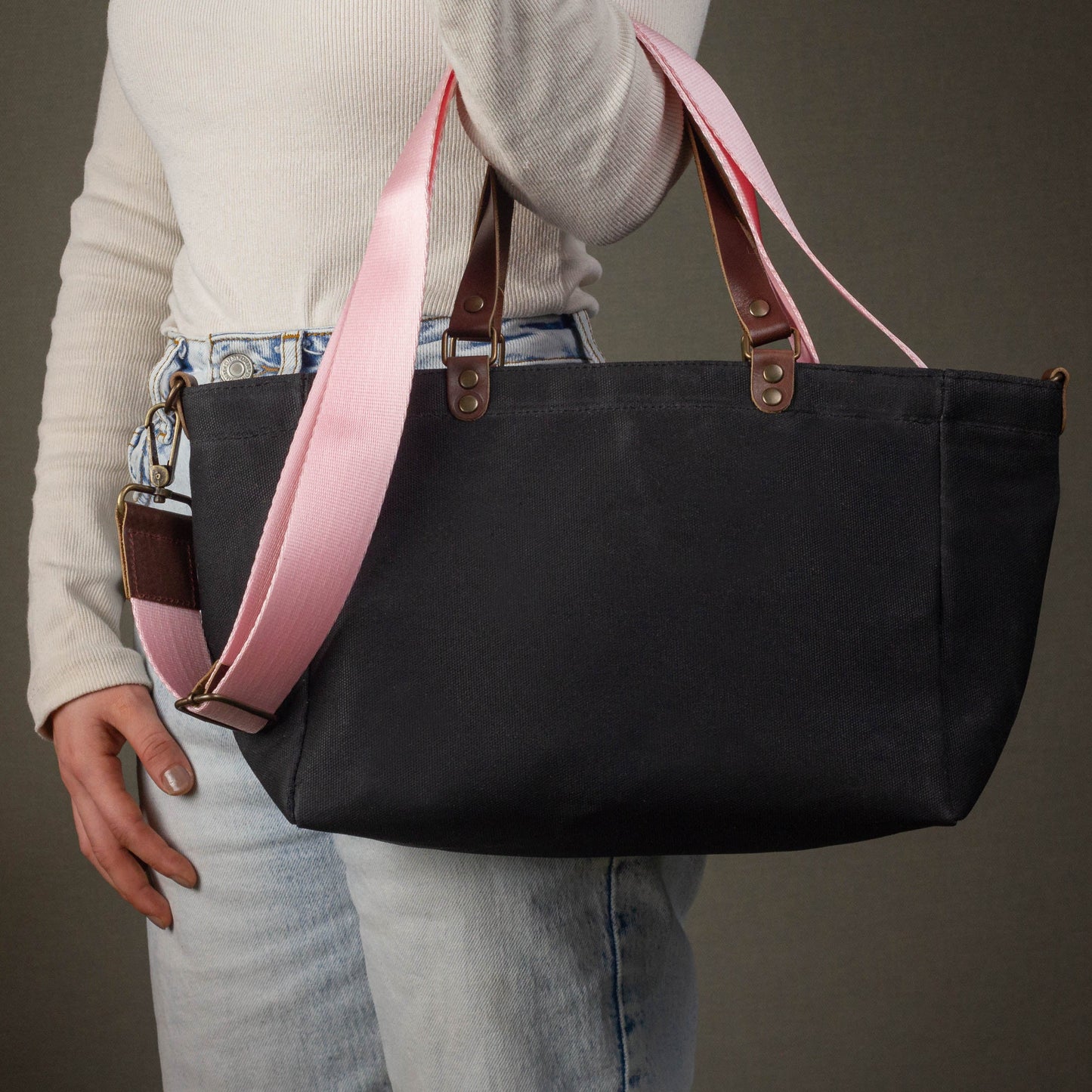 Person holding a black tote bag with pink straps against a neutral background