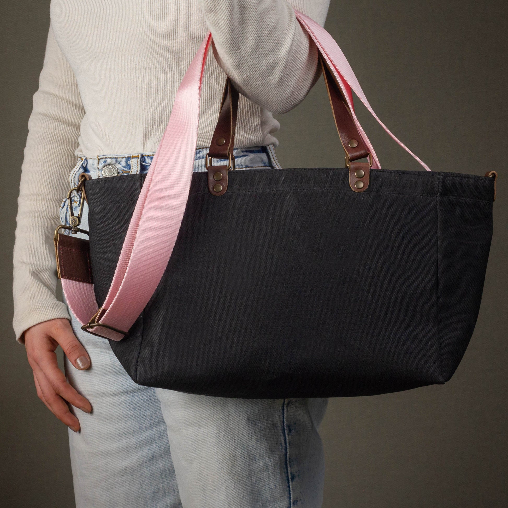 Person holding a black tote bag with pink straps against a neutral background