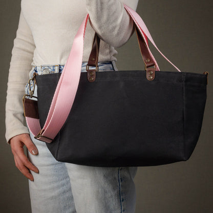 Person holding a black tote bag with pink straps against a neutral background